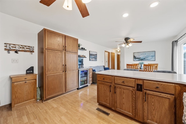 kitchen with light countertops, wine cooler, a ceiling fan, and light wood-style floors