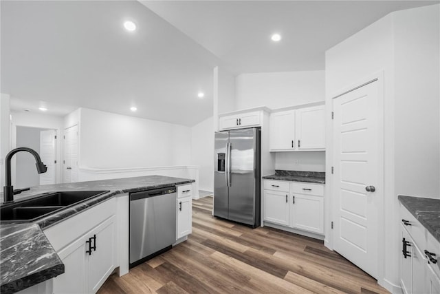 kitchen with lofted ceiling, appliances with stainless steel finishes, wood finished floors, white cabinetry, and a sink