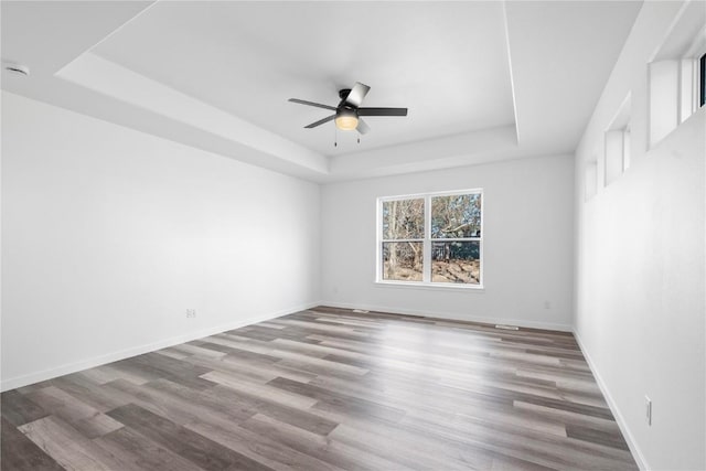 empty room featuring a raised ceiling, ceiling fan, baseboards, and wood finished floors