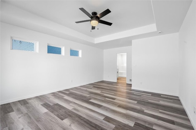 unfurnished room with wood finished floors, a raised ceiling, a ceiling fan, and baseboards