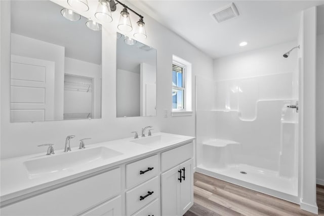 full bath featuring visible vents, a sink, a shower stall, and wood finished floors