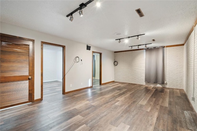 empty room featuring visible vents, a textured ceiling, brick wall, wood finished floors, and baseboards