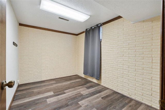 empty room featuring brick wall, a textured ceiling, visible vents, and dark wood-style flooring