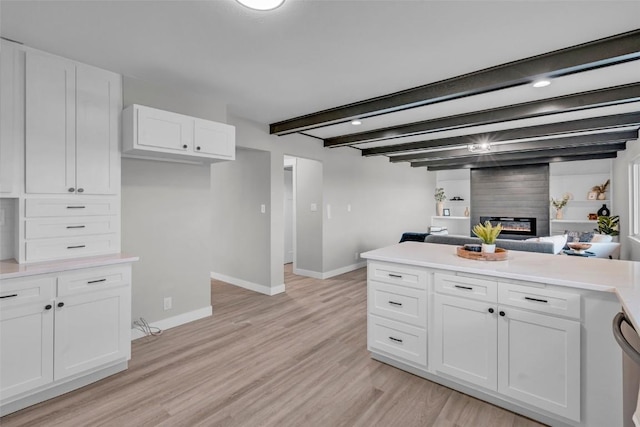 kitchen with light wood finished floors, baseboards, beamed ceiling, light countertops, and white cabinetry