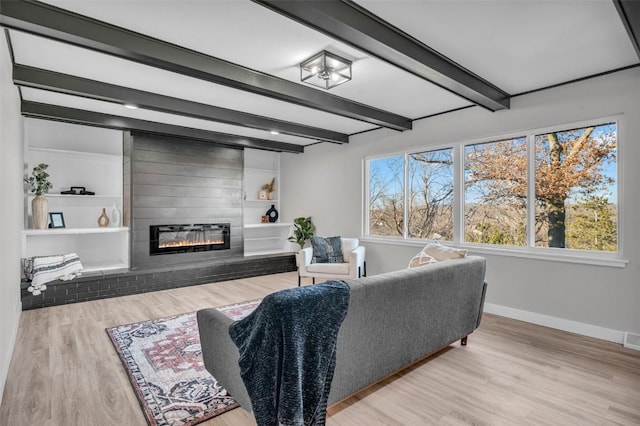 living area with a fireplace, visible vents, wood finished floors, beamed ceiling, and baseboards