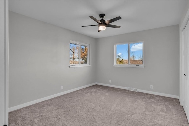 carpeted spare room with visible vents, ceiling fan, and baseboards