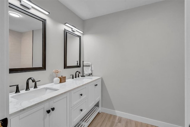 full bathroom featuring double vanity, baseboards, a sink, and wood finished floors