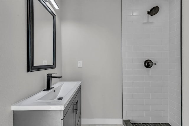 full bathroom featuring tiled shower, vanity, and baseboards