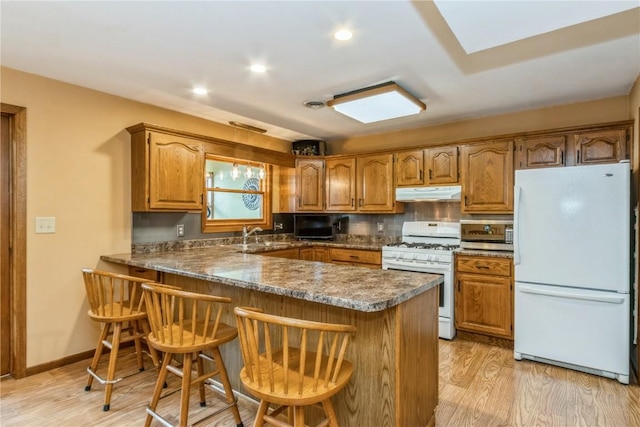 kitchen with a peninsula, white appliances, brown cabinetry, and under cabinet range hood