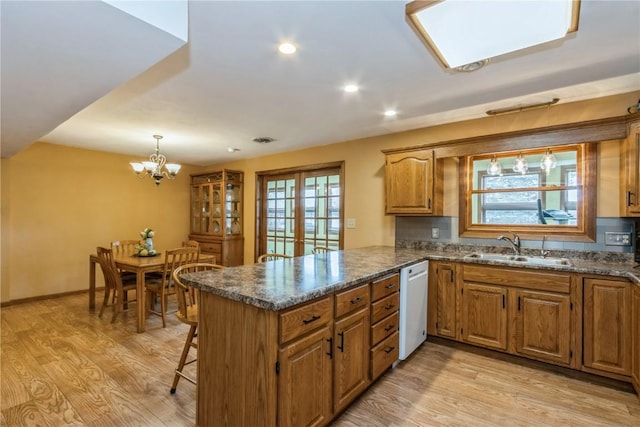 kitchen with brown cabinetry, dishwasher, a peninsula, and a sink