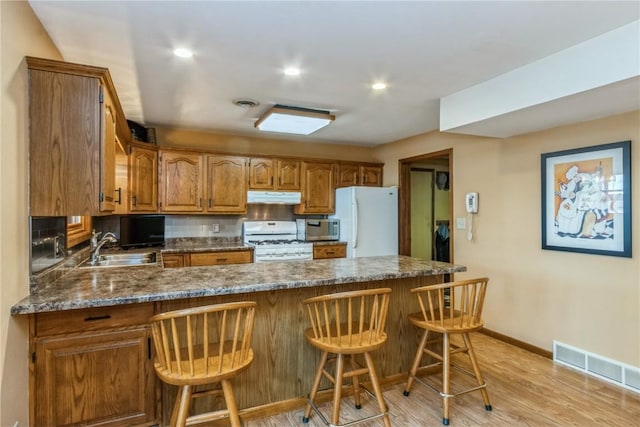 kitchen featuring visible vents, under cabinet range hood, a peninsula, white appliances, and a sink