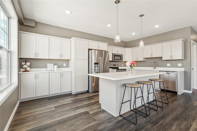 kitchen featuring dark wood finished floors, stainless steel appliances, light countertops, white cabinets, and a kitchen island