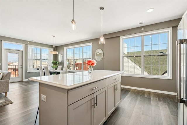 kitchen with decorative light fixtures, dark wood finished floors, light countertops, a kitchen island, and baseboards