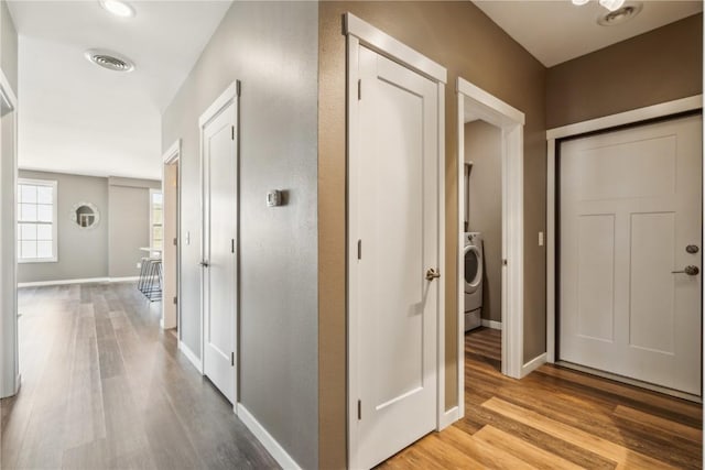 hall featuring baseboards, visible vents, washer / dryer, and light wood-style floors