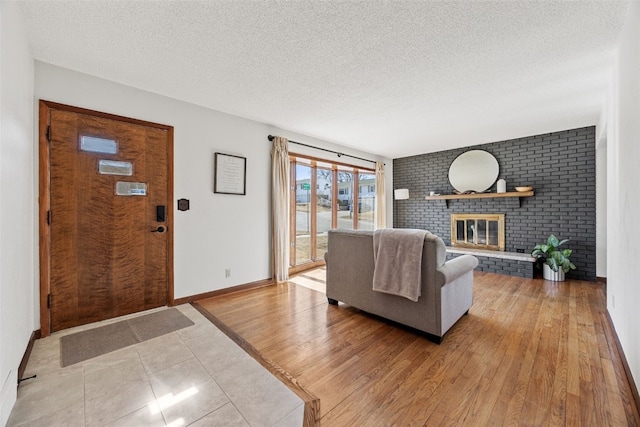 living room with a textured ceiling, light wood-type flooring, a brick fireplace, and baseboards