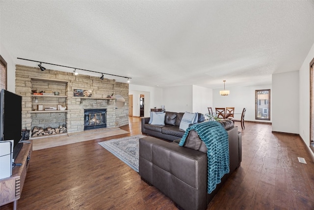 living area with a textured ceiling, wood finished floors, and a stone fireplace