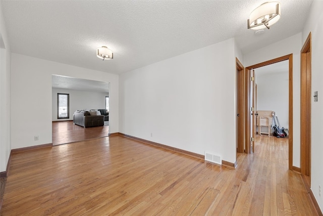 spare room featuring light wood-type flooring, visible vents, a textured ceiling, and baseboards