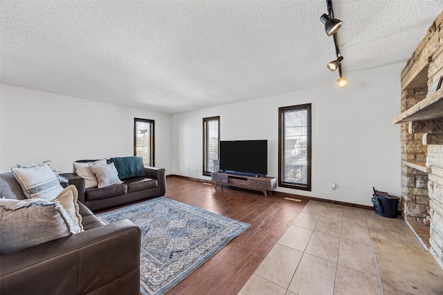 living room with baseboards, a stone fireplace, a textured ceiling, and wood finished floors