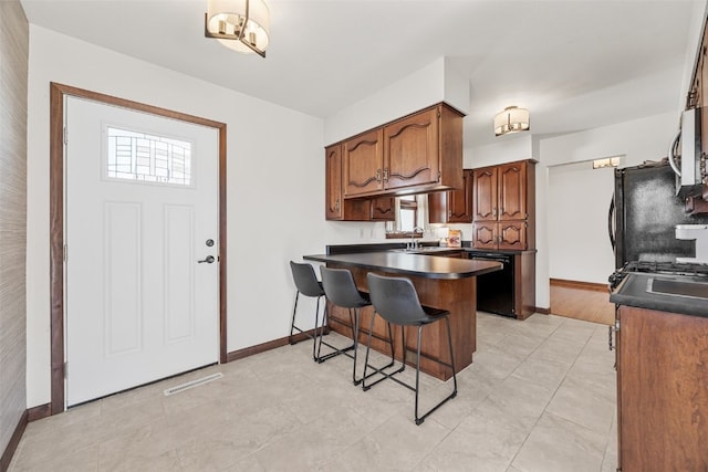 kitchen with a peninsula, a sink, a kitchen breakfast bar, black appliances, and dark countertops