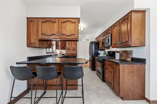 kitchen with dark countertops, a peninsula, black appliances, a kitchen bar, and a sink