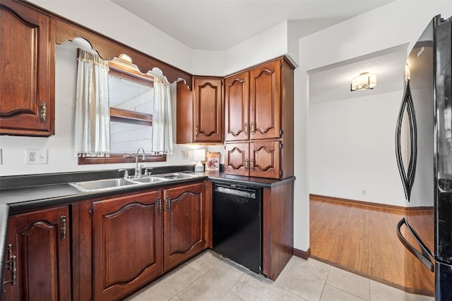 kitchen featuring a sink, baseboards, black dishwasher, freestanding refrigerator, and dark countertops