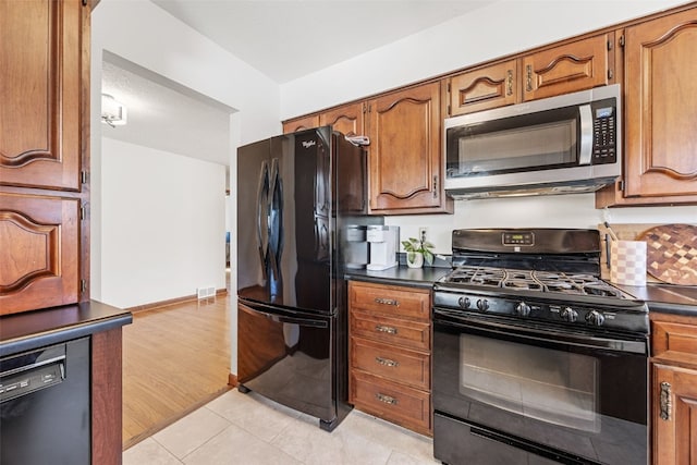 kitchen with light tile patterned floors, baseboards, black appliances, brown cabinetry, and dark countertops