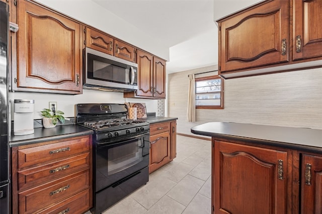 kitchen with light tile patterned floors, dark countertops, stainless steel microwave, brown cabinets, and black gas stove