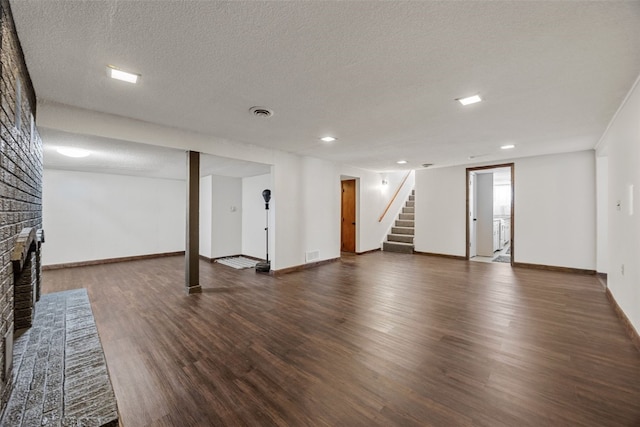 finished basement featuring a textured ceiling, a fireplace, wood finished floors, visible vents, and stairway