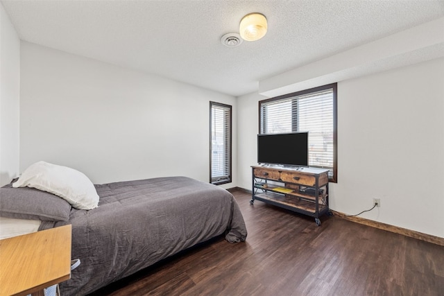 bedroom featuring a textured ceiling, wood finished floors, visible vents, and baseboards