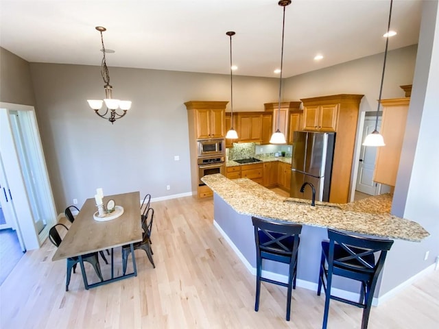 kitchen with light stone counters, stainless steel appliances, brown cabinetry, a sink, and a peninsula