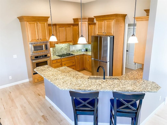 kitchen featuring stainless steel appliances, a sink, a peninsula, and light stone counters