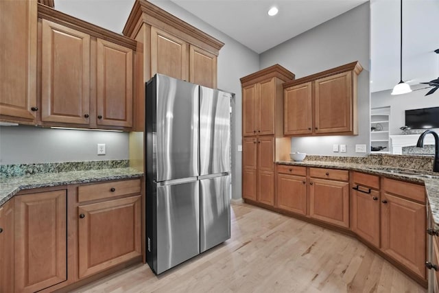 kitchen featuring stone counters, a sink, freestanding refrigerator, and light wood-style floors