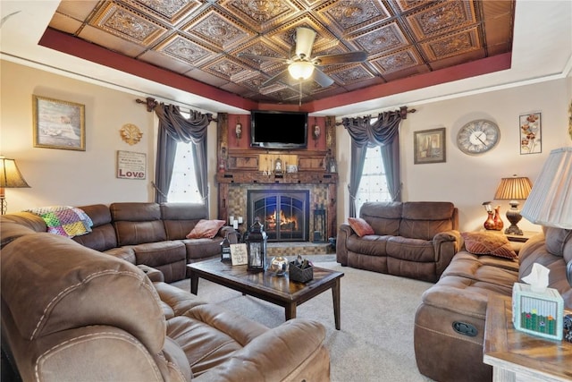 living room with a stone fireplace, a tray ceiling, carpet, and an ornate ceiling