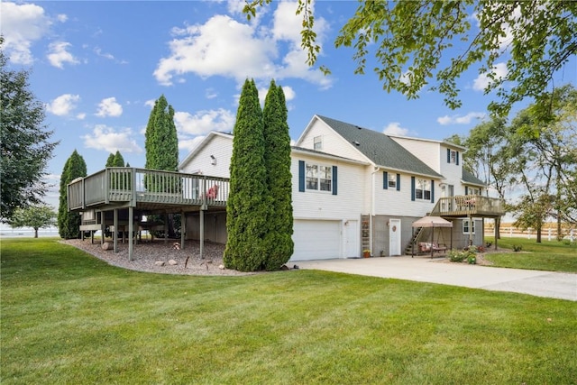 rear view of property featuring a garage, concrete driveway, a lawn, and a wooden deck