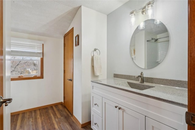 bathroom with a textured ceiling, baseboards, wood finished floors, and vanity