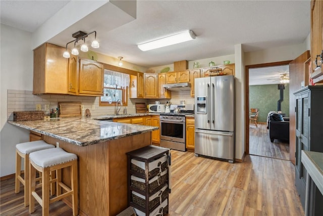 kitchen with light wood finished floors, stainless steel appliances, a wood stove, under cabinet range hood, and a peninsula