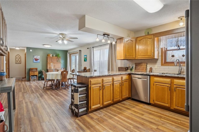 kitchen featuring light wood finished floors, backsplash, a peninsula, stainless steel dishwasher, and a sink