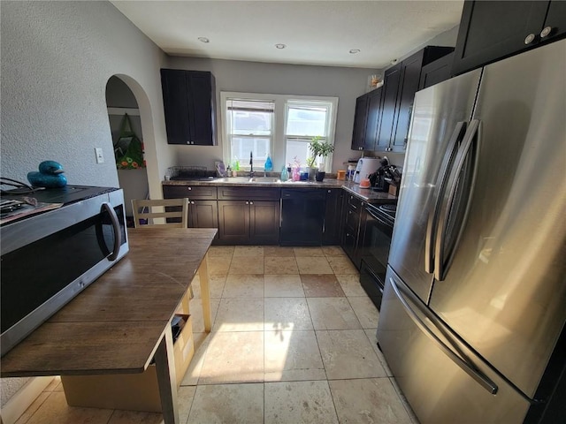 kitchen with dark countertops, a textured wall, a sink, dark cabinets, and black appliances