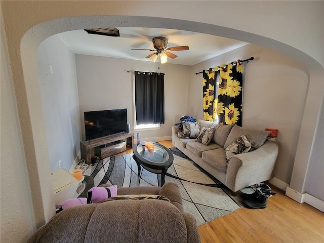 living room featuring arched walkways, ceiling fan, baseboards, and wood finished floors