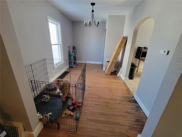 corridor with arched walkways, a notable chandelier, visible vents, baseboards, and light wood-style floors