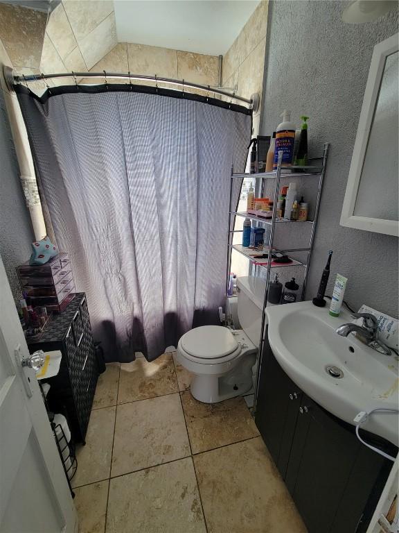 full bath with a textured wall, tile patterned flooring, toilet, shower / tub combo, and vanity