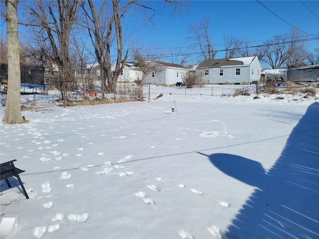 snowy yard with a trampoline, a residential view, and fence