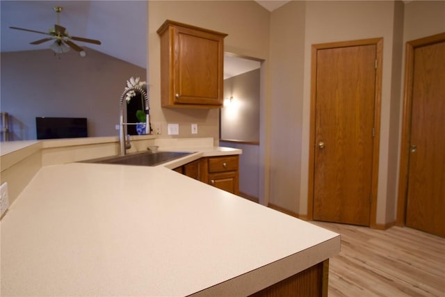 kitchen featuring brown cabinets, a peninsula, light countertops, light wood-type flooring, and a sink