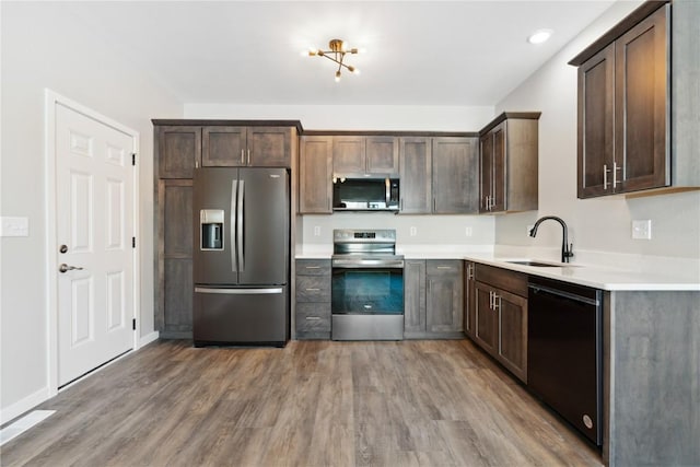 kitchen featuring appliances with stainless steel finishes, light wood-style floors, a sink, and dark brown cabinetry