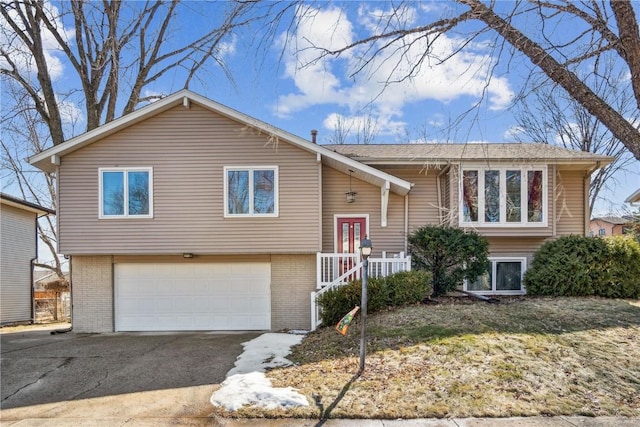 raised ranch with an attached garage, aphalt driveway, and brick siding