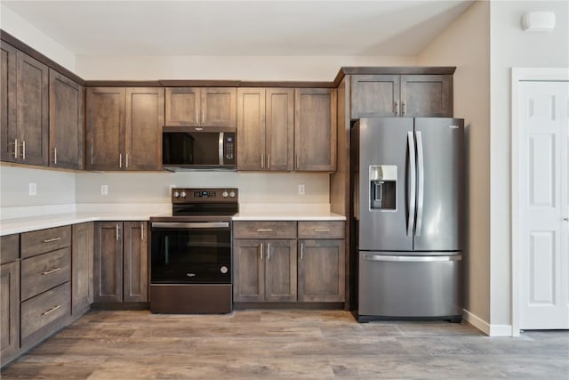 kitchen with appliances with stainless steel finishes, light countertops, light wood-style flooring, and dark brown cabinets