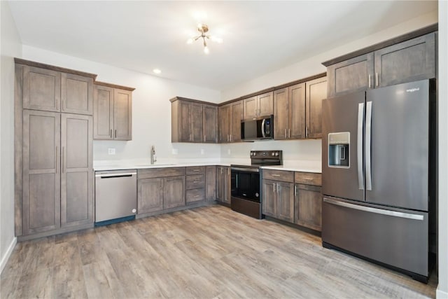 kitchen featuring stainless steel appliances, a sink, dark brown cabinets, light countertops, and light wood-type flooring