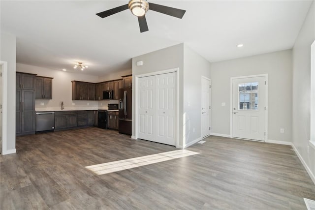 kitchen with dark brown cabinetry, dark wood-type flooring, baseboards, light countertops, and black appliances