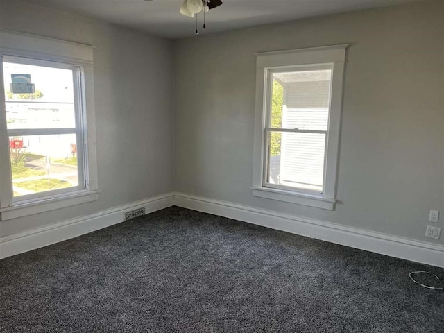 spare room with dark colored carpet, visible vents, plenty of natural light, and baseboards