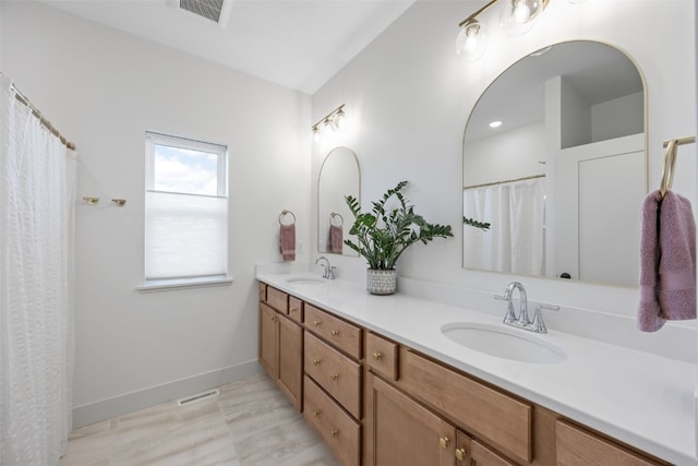 bathroom with double vanity, baseboards, visible vents, and a sink